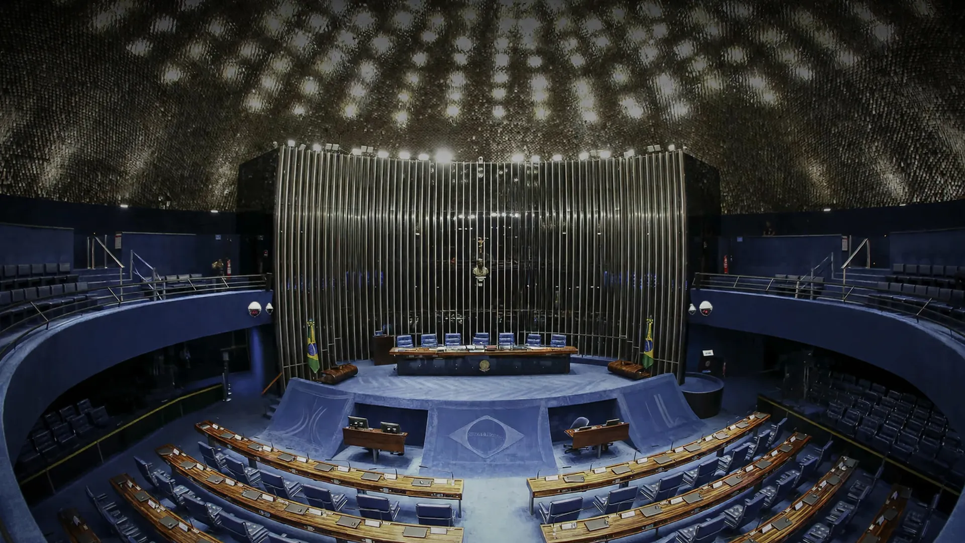 Plenário vazio do Senado Federal com câmeras de segurança e cadeiras azuis em semicírculo, simbolizando a nueva lei de monitoramento eletrônico para agressores