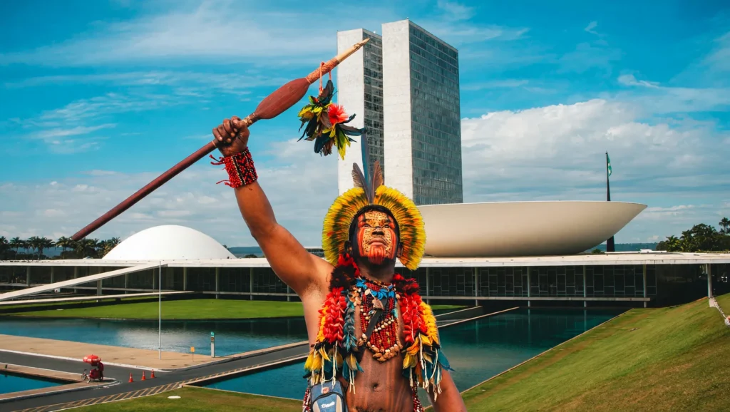 Líder indígena em traje ritual com Brasília ao fundo, símbolo da universidade federal indígena Brasil