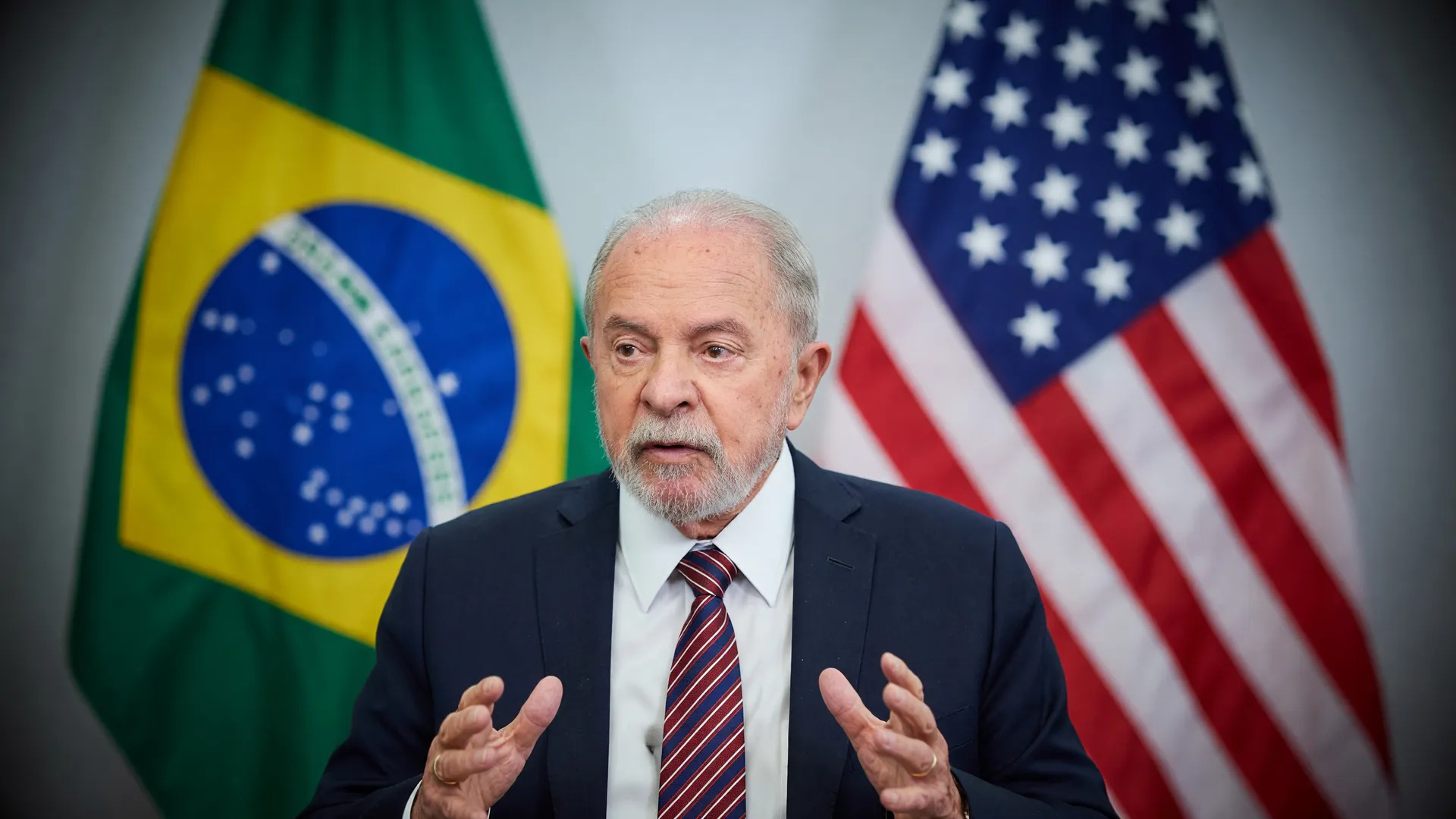 Lula em primeiro plano com bandeiras do Brasil e dos EUA ao fundo, remetendo à decisão sobre tarifas ao Brasil