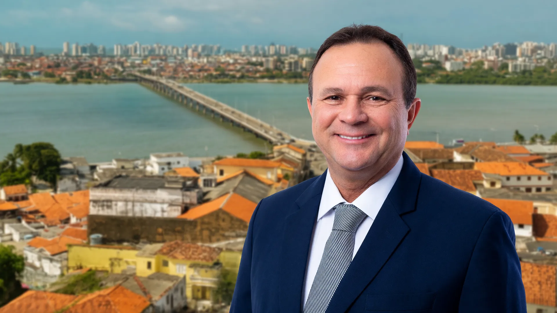 Carlos Brandão sorridente com vista aérea de São Luís ao fundo, simbolizando as promessas de Carlos Brandão no Maranhão