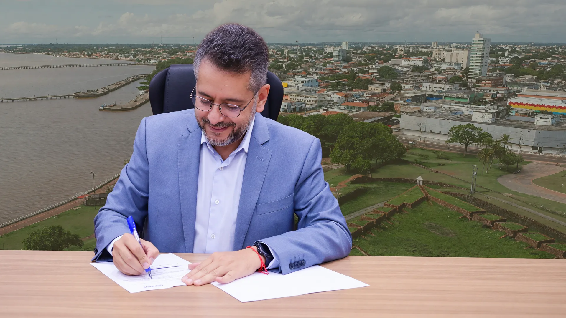 Clécio Luís assina documentos em gabinete, com Macapá ao fundo, refletindo as promessas de Clécio Luís no Amapá