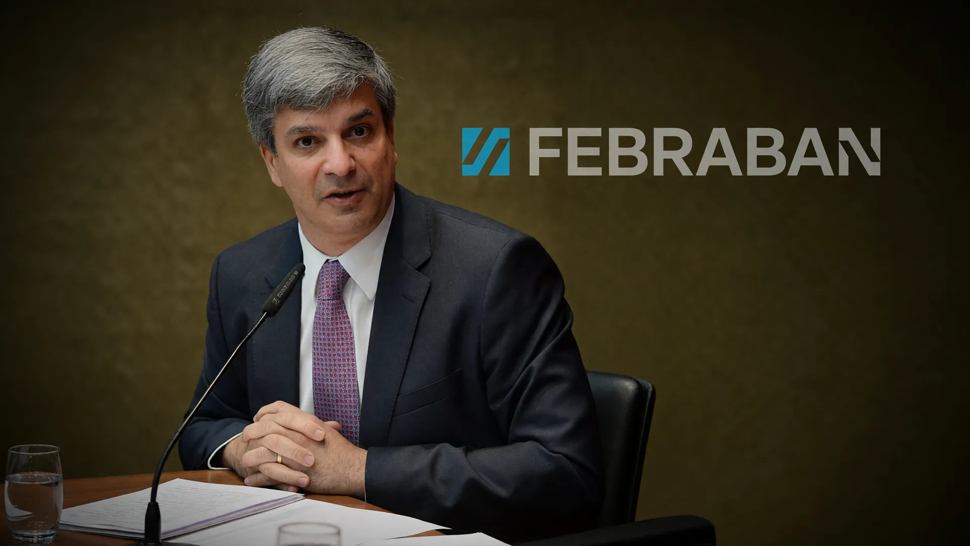 Leandro Vilain, novo presidente da Febraban, em traje formal com o logo da federação ao fundo