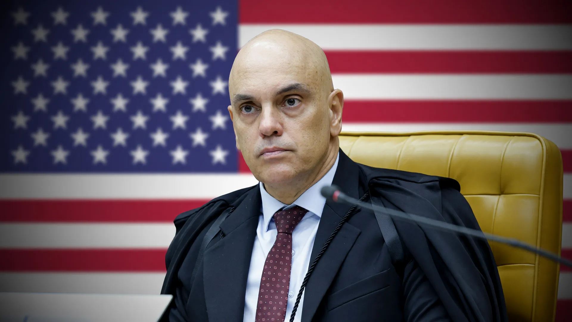 Alexandre de Moraes na cadeira do STF com bandeira dos EUA ao fundo, em cena sobre sanções contra Alexandre de Moraes