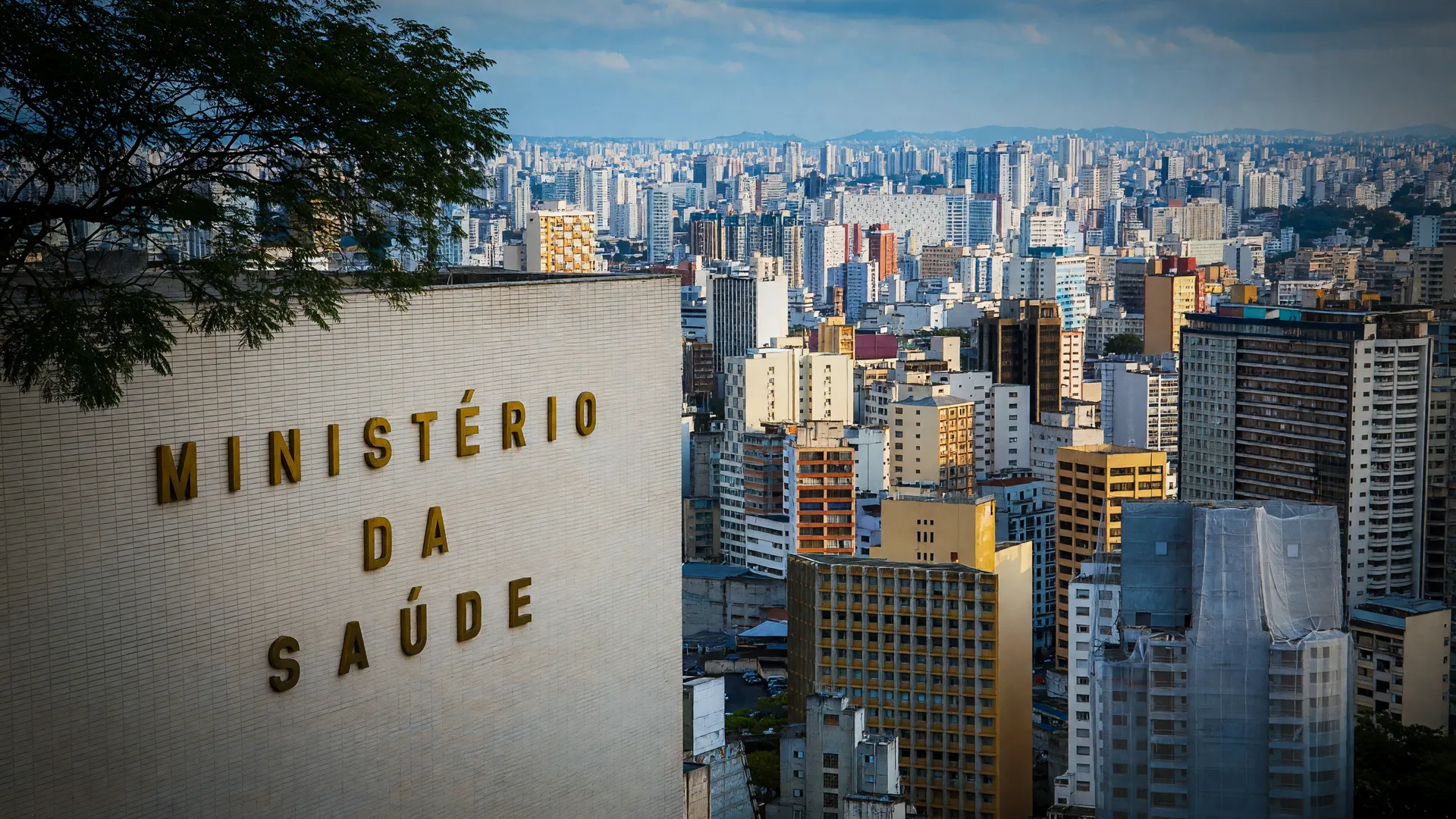Skyline de São Paulo e sede do Ministério da Saúde, em referência ao surto de sarampo em São Paulo
