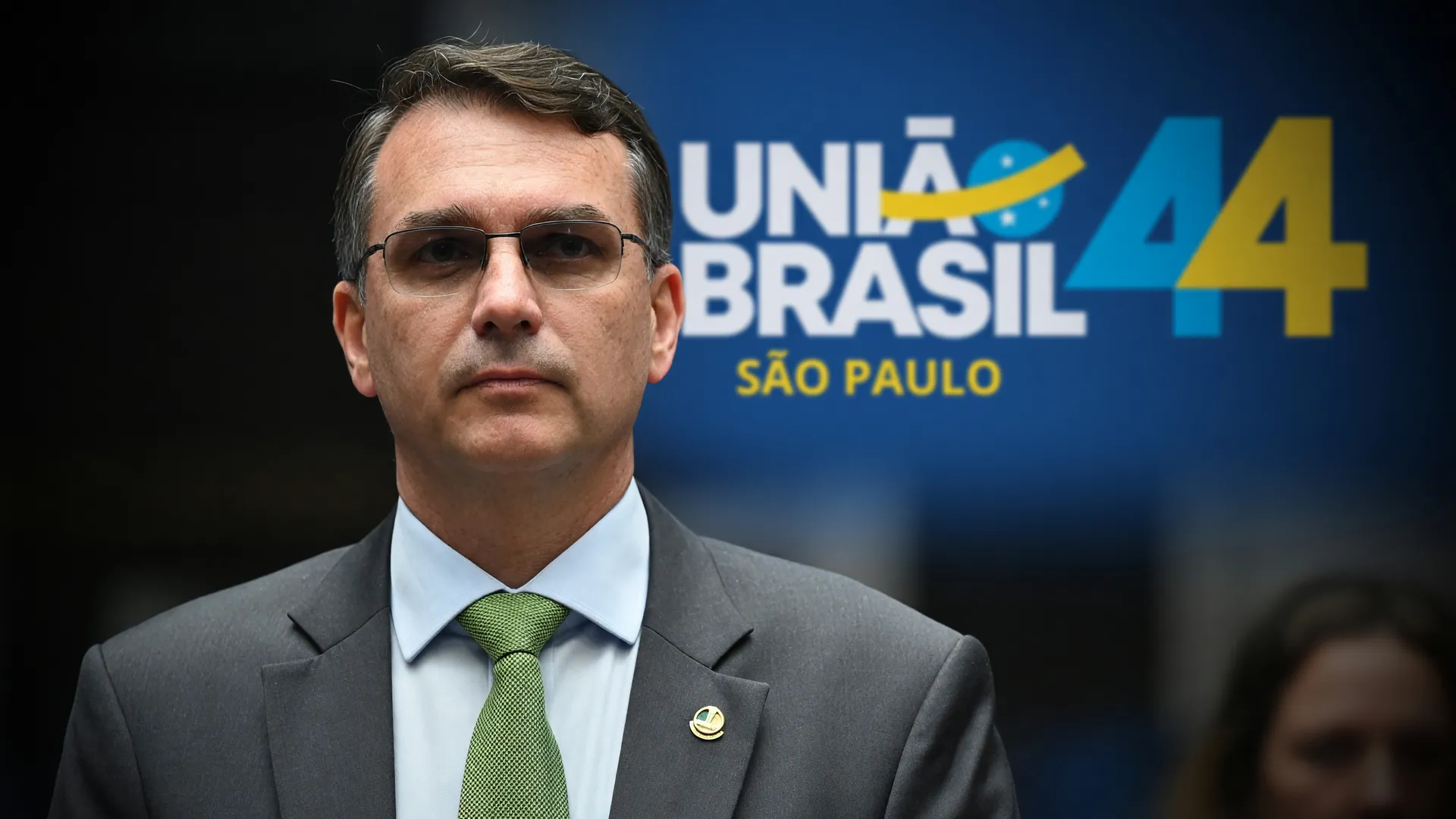 Flávio Bolsonaro isolado diante da sigla da União Brasil — neutralidade na eleição presidencial 2026