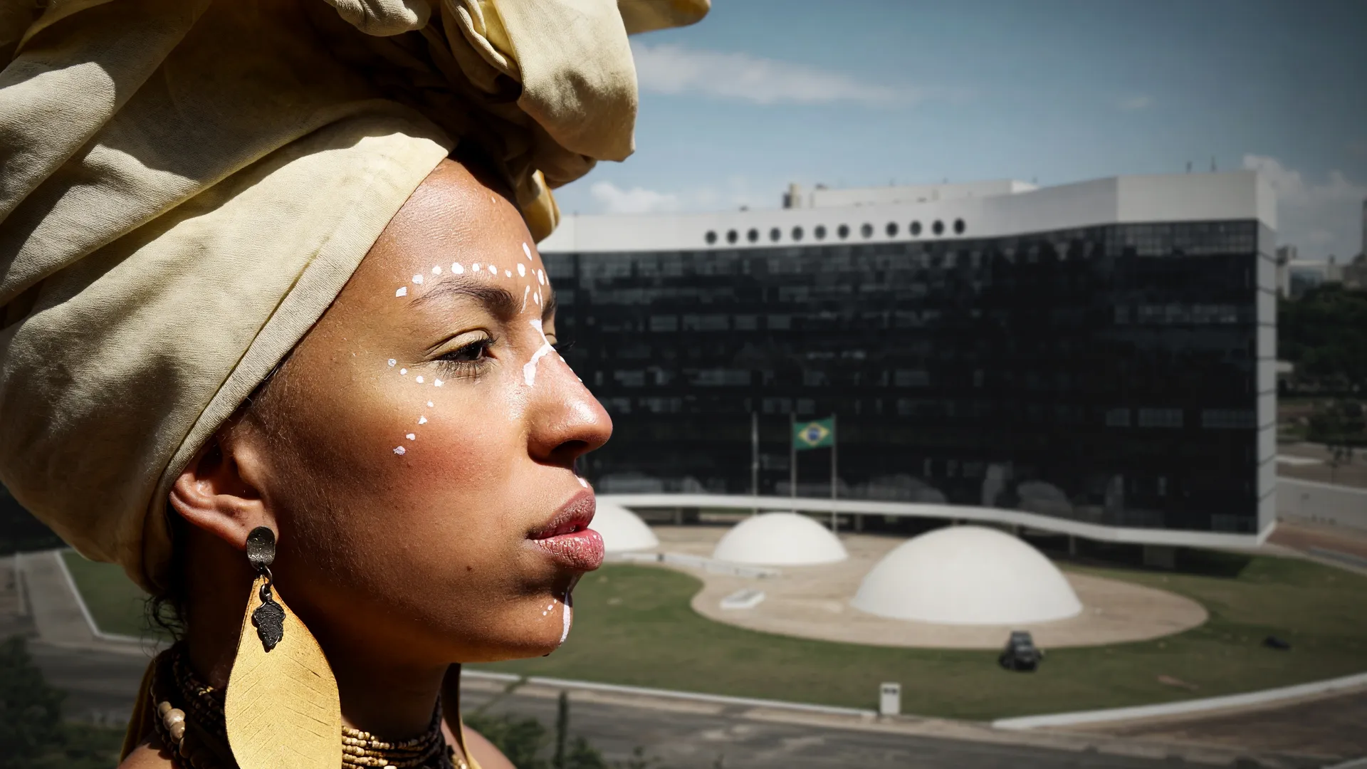 Mulher negra com turbante dourado e prédio do TSE ao fundo, representando candidatas a deputada federal SP