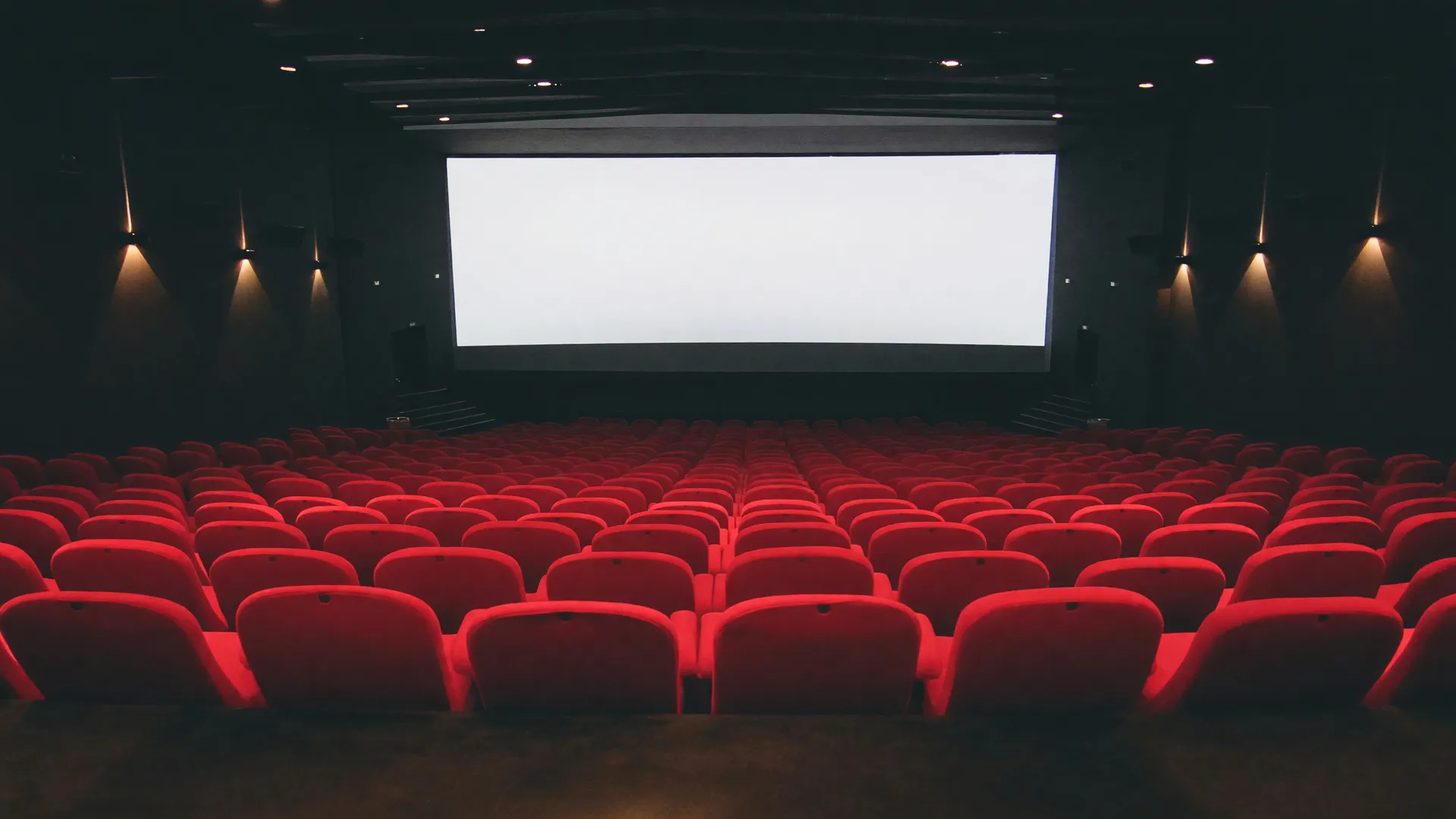 Sala de cinema vazia com poltronas vermelhas e tela branca, simbolizando a falta de acesso gratuito à cultura