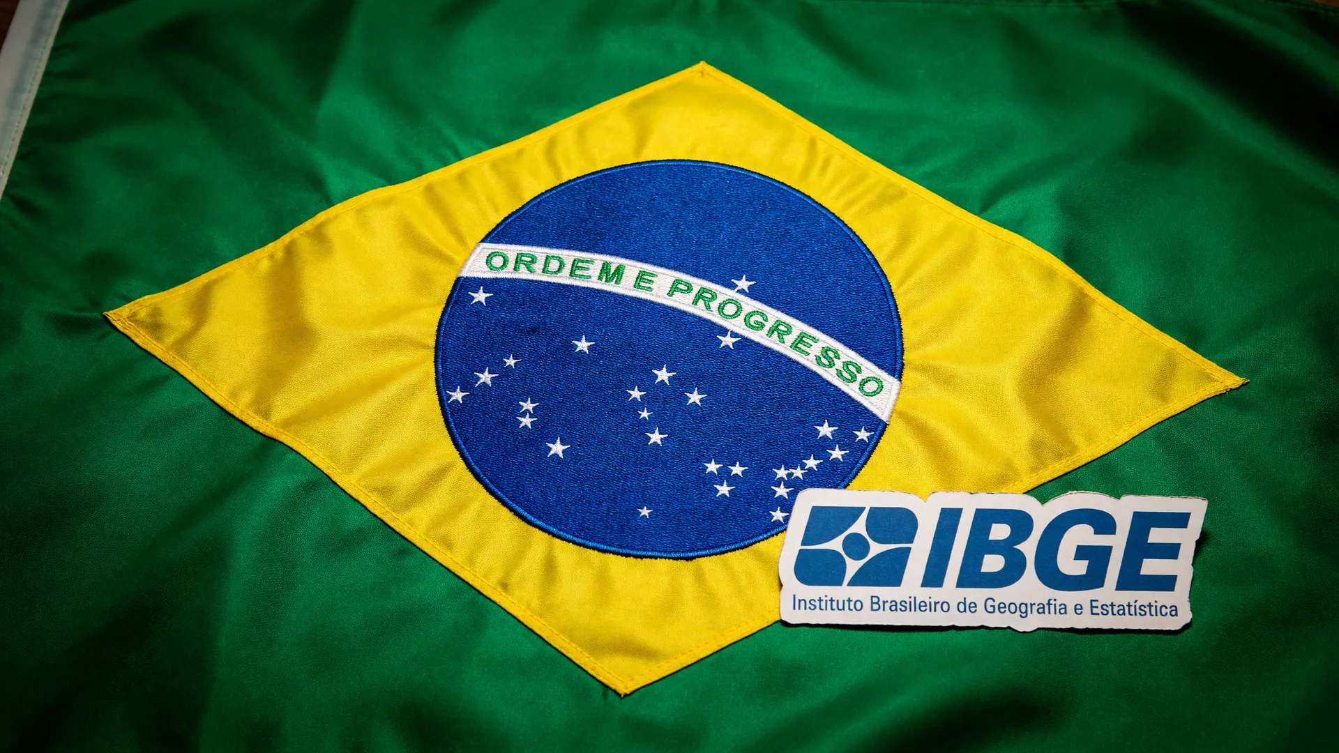 Bandeira do Brasil e logotipo do IBGE ilustram a queda da taxa de desemprego terceiro trimestre para 5,2%
